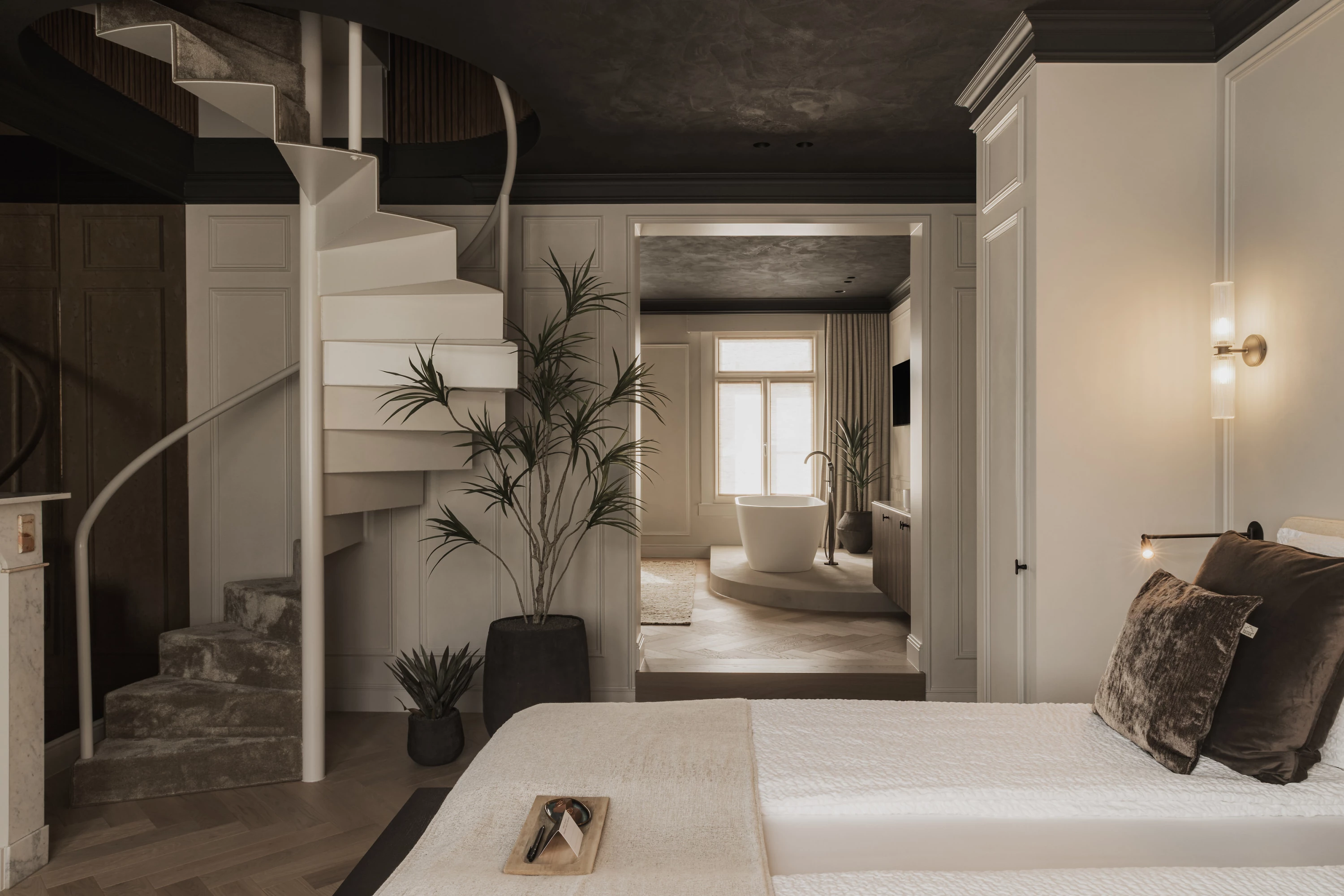 Zicht op bed met draaitrap naar badkamer en doorgang naar ontspanningsruimte met relax bad in kamer H&eacute;ritage (BnB Herenhuis Izegem)