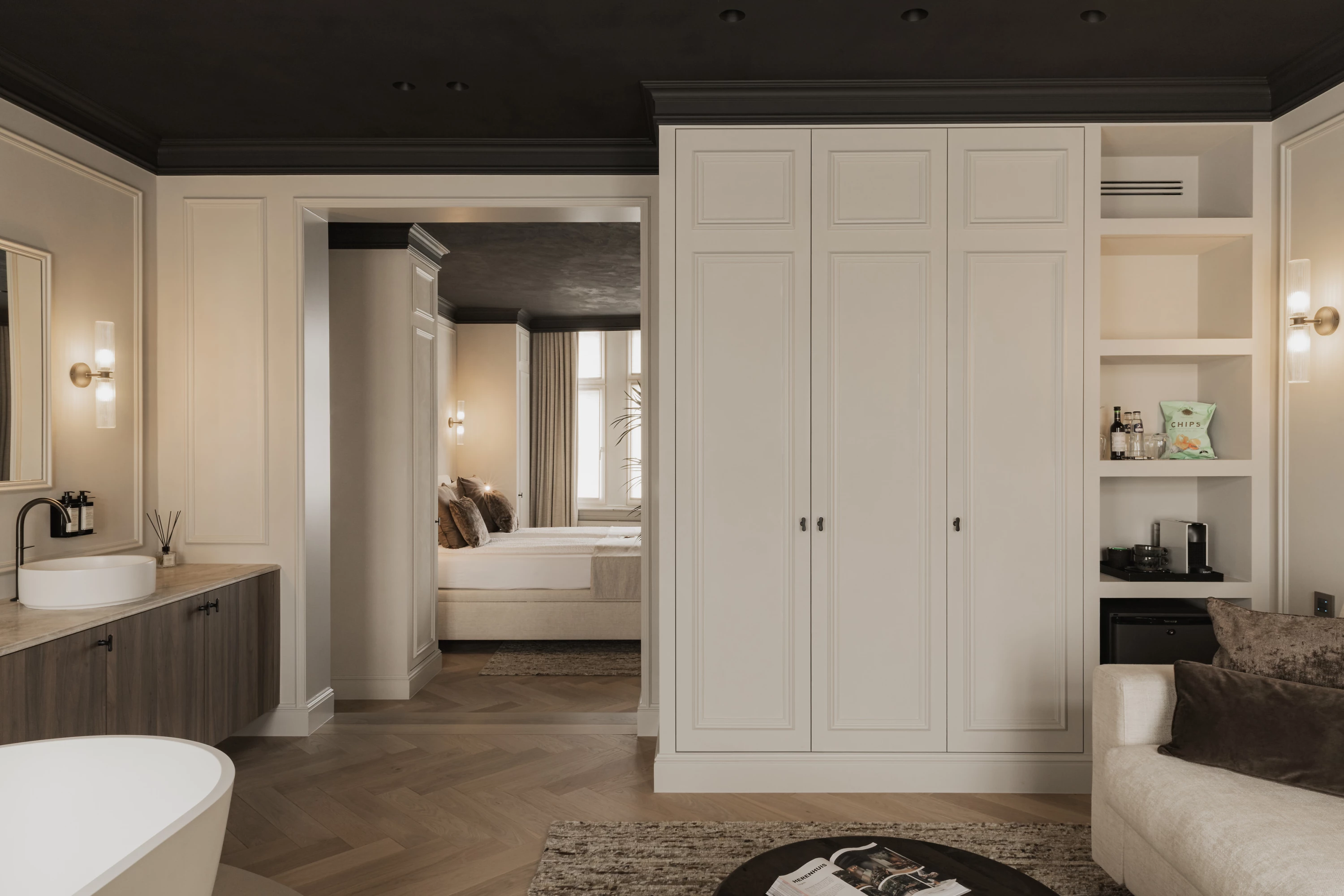 Zicht vanuit ontspanningsruimte met relax bad, wastafel en zitbank op slaapkamer H&eacute;ritage (B&B Herenhuis regio Roeselare - Kortrijk)
